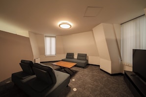 A modern hotel room with a sofa, two armchairs, a small table, and a TV.