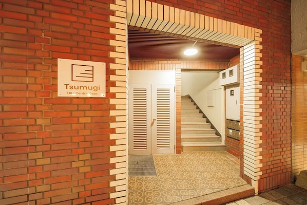 A Tsumugi Hita Central Base entrance with a brick wall, a tiled floor, and a staircase leading inside.