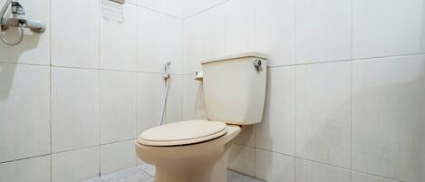 Des toilettes dans une salle de bain aux murs recouverts de carreaux blancs, avec une pomme de douche fixée au mur.
