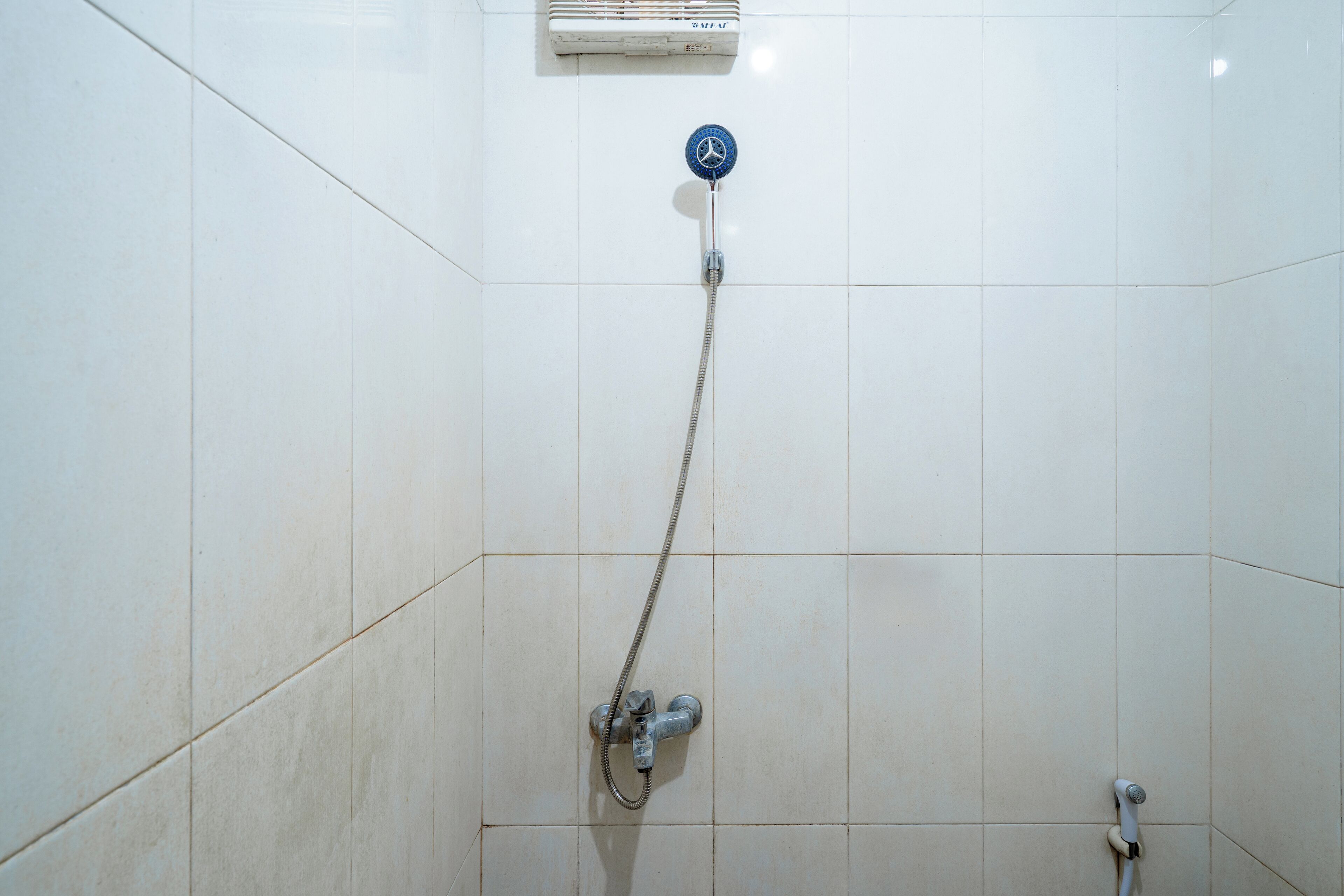 A shower with a handheld showerhead and a wall-mounted control panel.