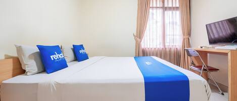 A neatly made bed with blue and white bedding, a television on a wooden desk, and a window with curtains.
