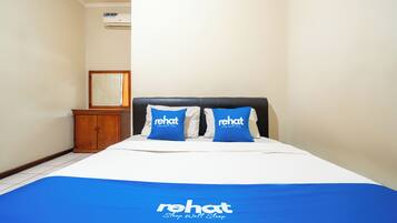 A bedroom with a bed, two pillows with 'rehat' branding, a wooden cabinet, and a framed picture on the wall.