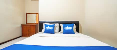 A bedroom with a bed, two pillows with 'rehat' branding, a wooden cabinet, and a framed picture on the wall.