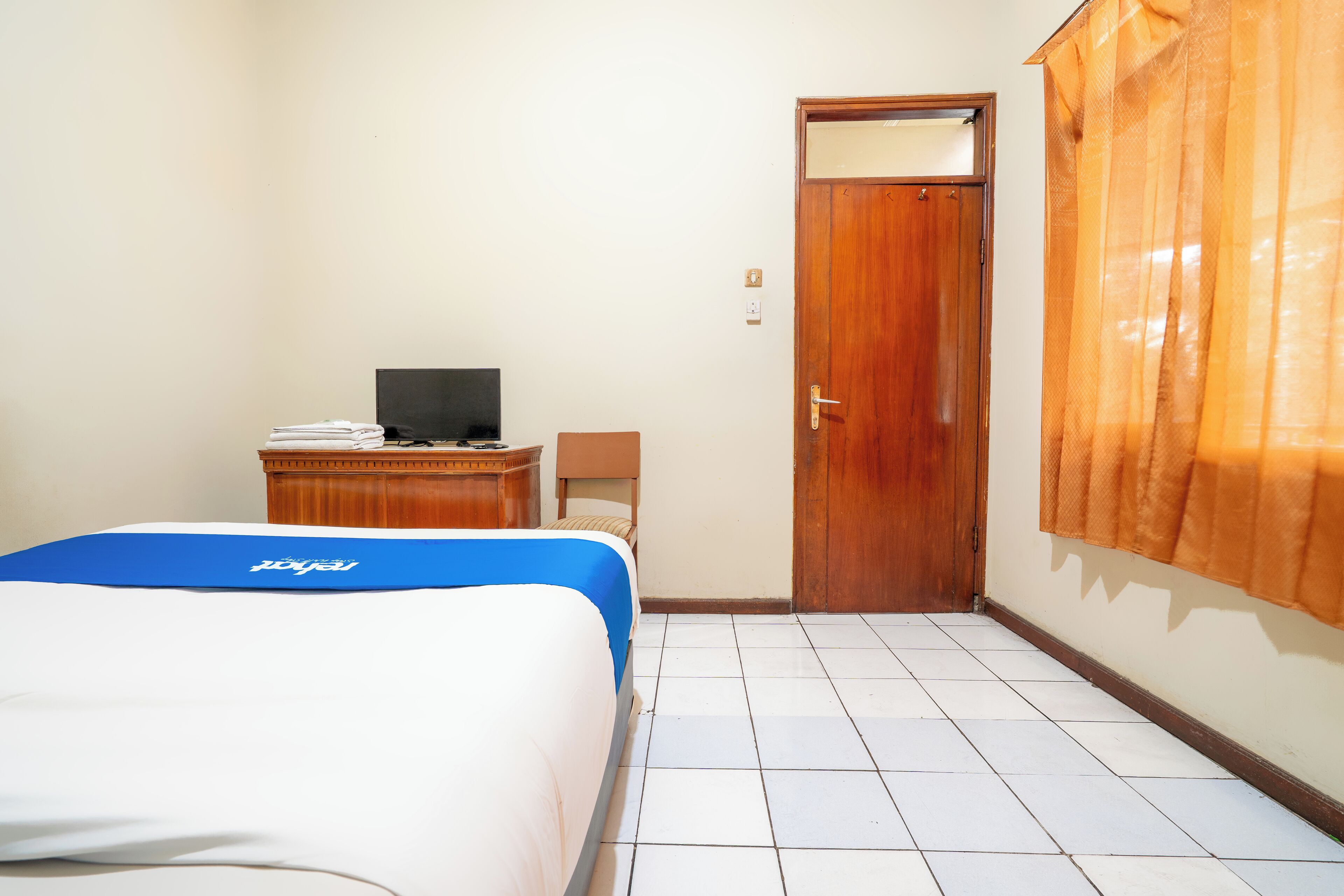 A hotel room with a bed, a desk with a computer, a wardrobe, and a door.