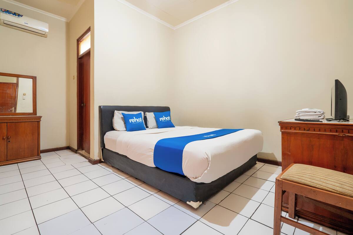 Une chambre d’hôtel comprenant un lit, une table de chevet en bois, une chaise et un bureau avec une autre chaise.
