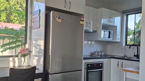 A modern kitchen with white cabinets, a stainless steel refrigerator, a microwave, and an oven. There is a dining table with chairs and a vase of flowers.