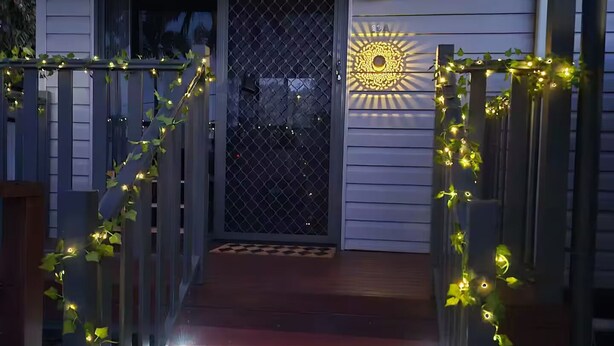 A wooden deck with a metal gate leading to a house entrance, decorated with string lights.