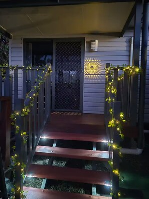 A wooden deck with a metal gate leading to a house entrance, decorated with string lights. - Convenient Getaway Home in Straithpine (Strathpine)