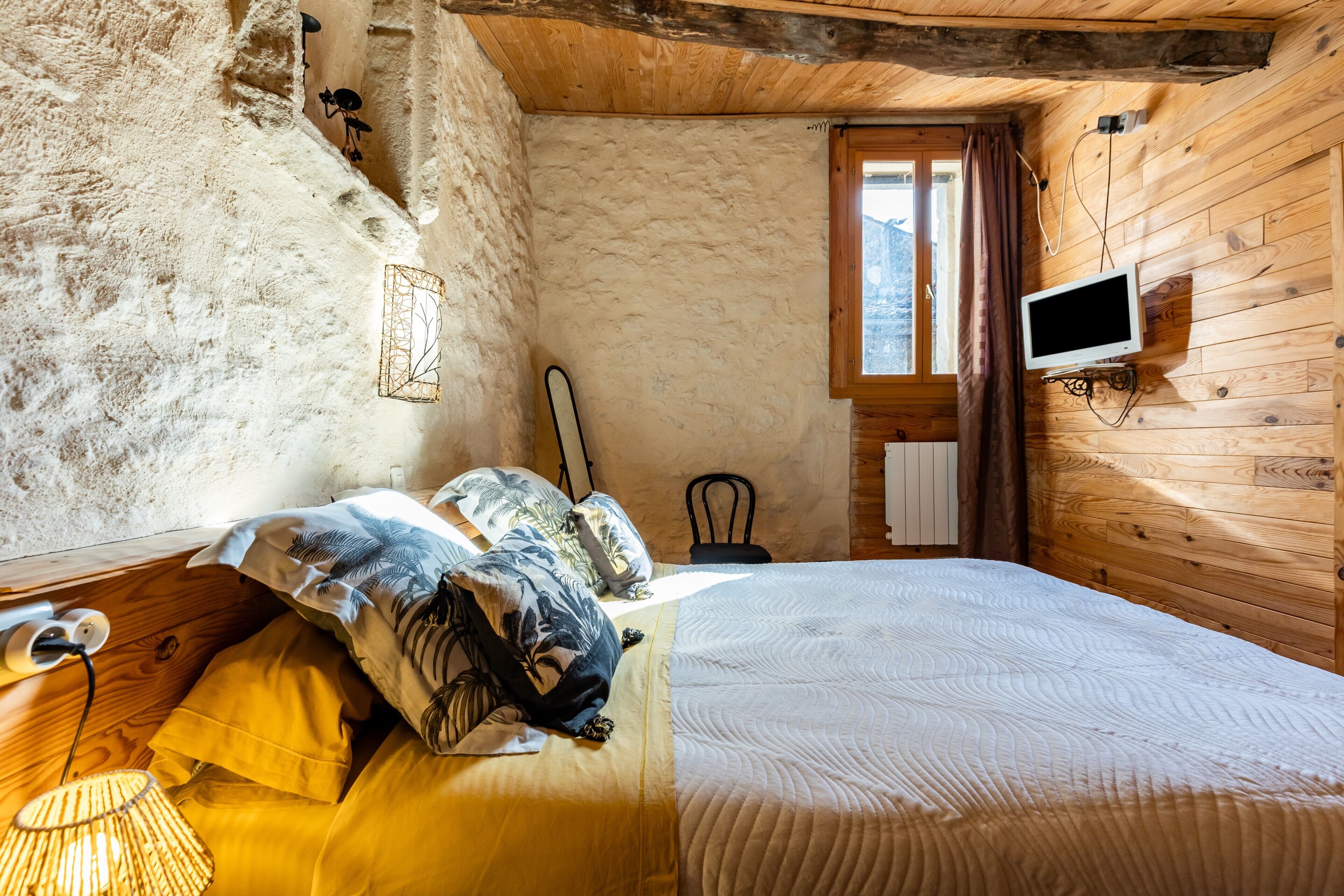 A bedroom with a bed, a television, a window, and a wooden ceiling.