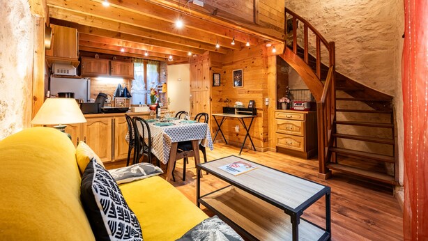 A cozy log cabin interior with a dining area, kitchen, and a staircase. - Saint François Apartment – Romantic Getaway (Monségur)
