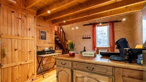 A wooden interior with a kitchen counter, a coffee machine, and a window with a red curtain. - Saint François Apartment – Romantic Getaway (Monségur)