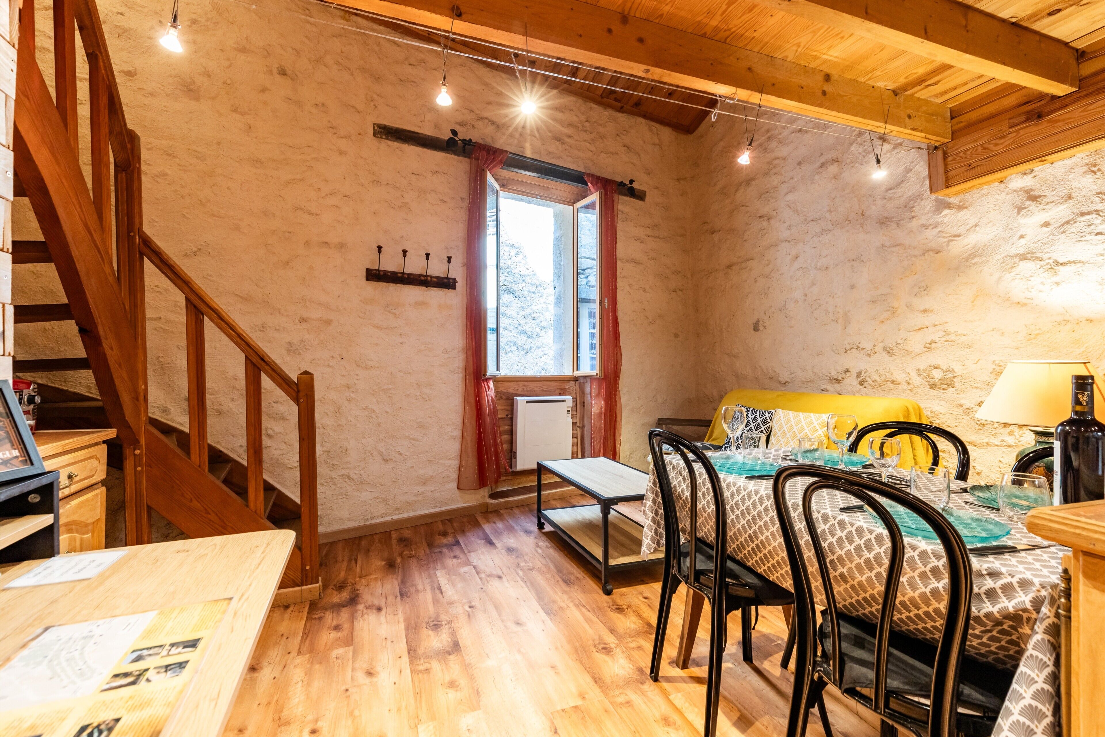 Une pièce rustique avec un escalier en bois, une table à manger avec des chaises, un canapé et une fenêtre avec des rideaux.