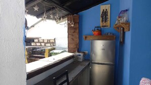 Une petite cuisine équipée d’un réfrigérateur, d’une étagère en bois sur laquelle est posée une théière, et d’un tableau accroché au mur.