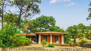 A two-story building with a tiled roof, surrounded by greenery and trees. - Maison accès plage direct (Les Mathes)