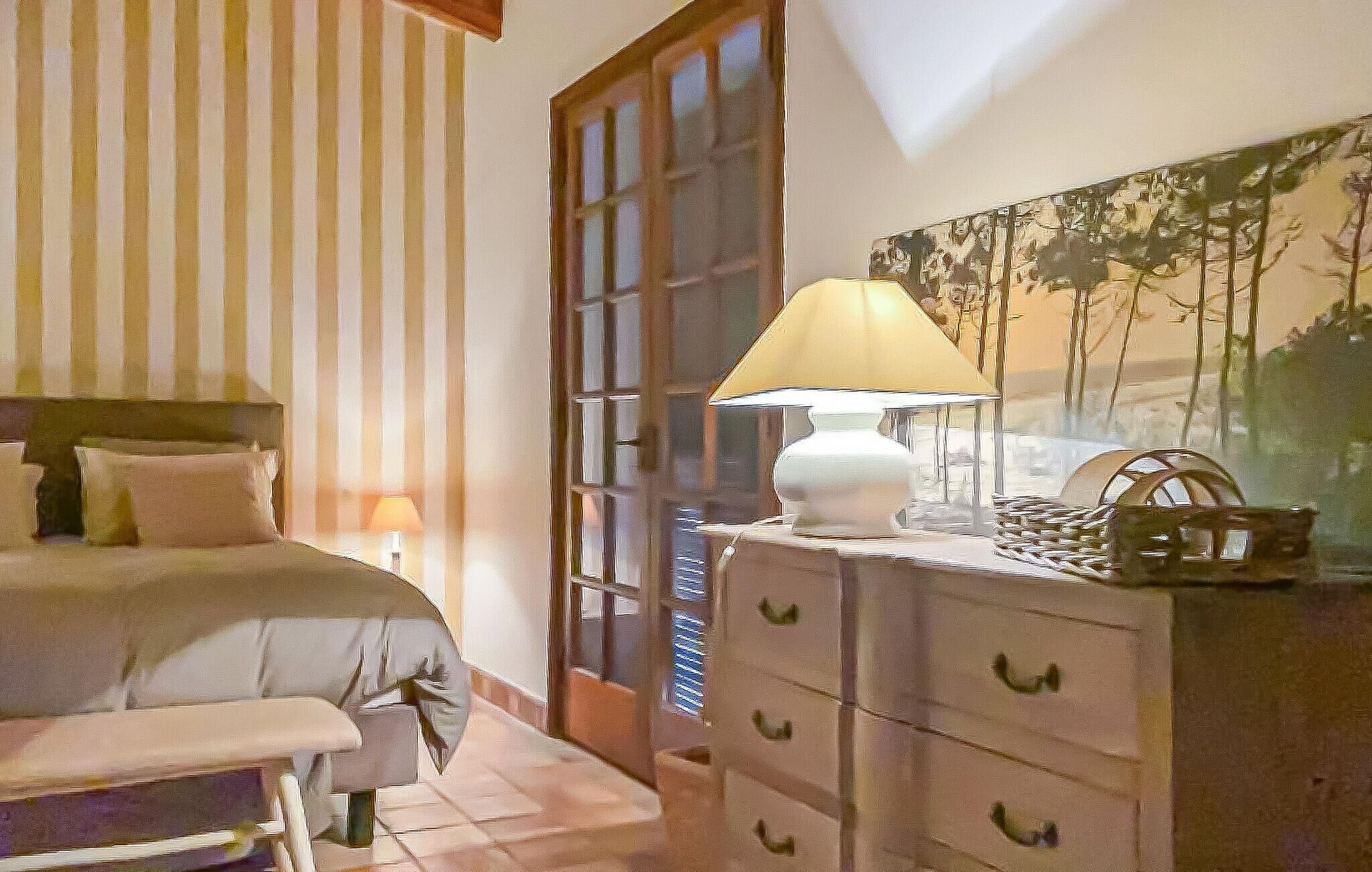 A bedroom with a bed, bedside table, lamp, dresser, and a painting on the wall.