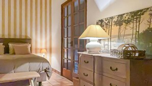 A bedroom with a bed, bedside table, lamp, dresser, and a painting on the wall. - Maison accès plage direct (Les Mathes)