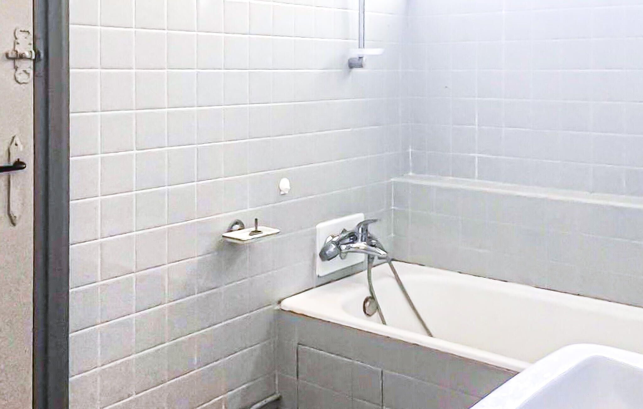 A bathroom with white tiled walls, a bathtub, and a shower.