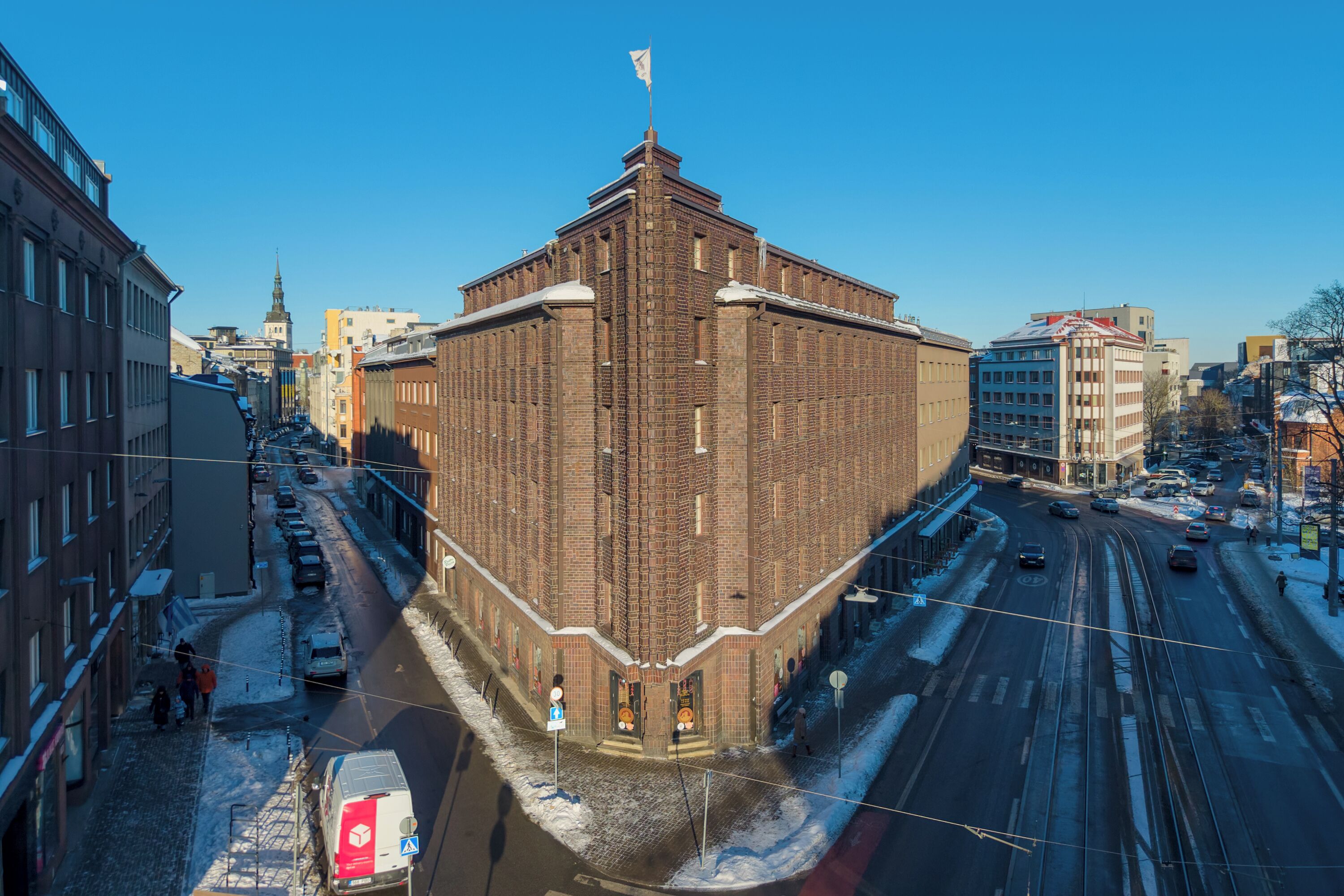 A corner building with a prominent corner, adjacent to a tram line and a street with parked cars.