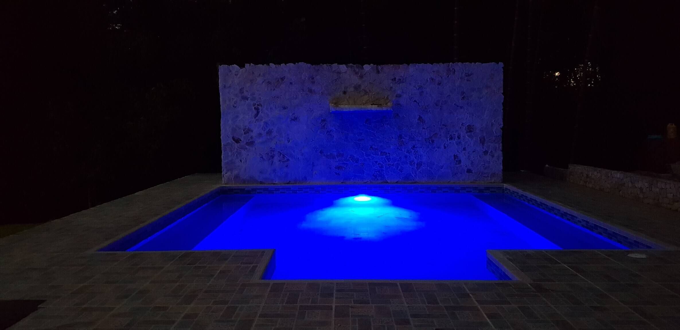 Une piscine avec un élément décoratif aquatique illuminé de lumière bleue la nuit.