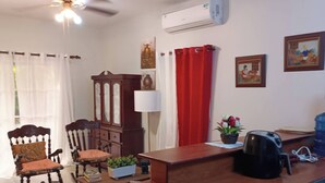 Ein gut beleuchteter Raum mit Deckenventilator, einem Holztisch mit Kaffeemaschine, einem Stuhl, einer Lampe und einem Blumentopf.