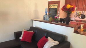 Ein dunkelbraunes Ledersofa mit roten und weißen Kissen, ein Wasserspender, eine Ananas und eine Vase mit Blumen auf einer Ablagefläche.