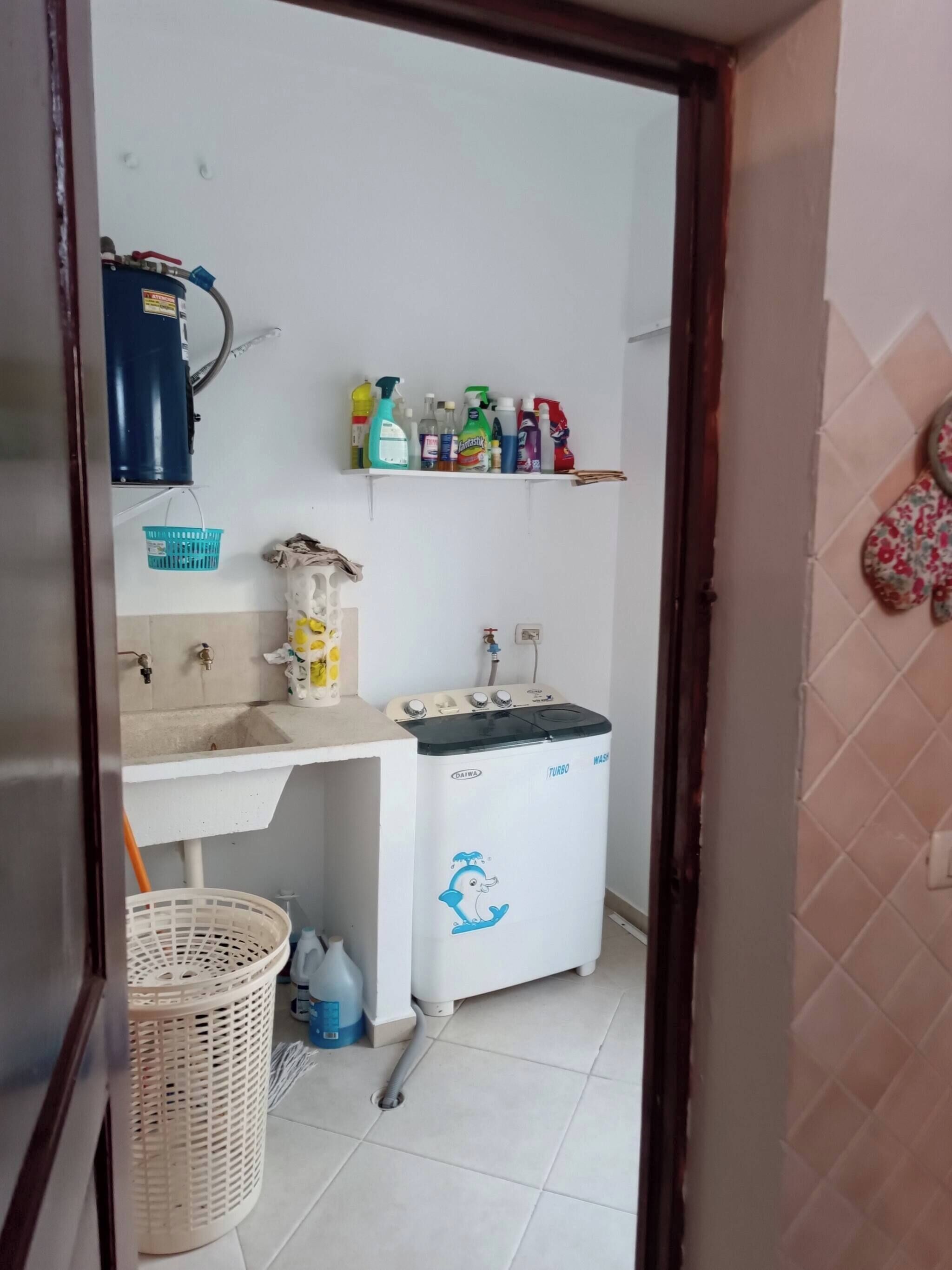 A compact kitchen with a sink, a washing machine, and a shelf with cleaning supplies.