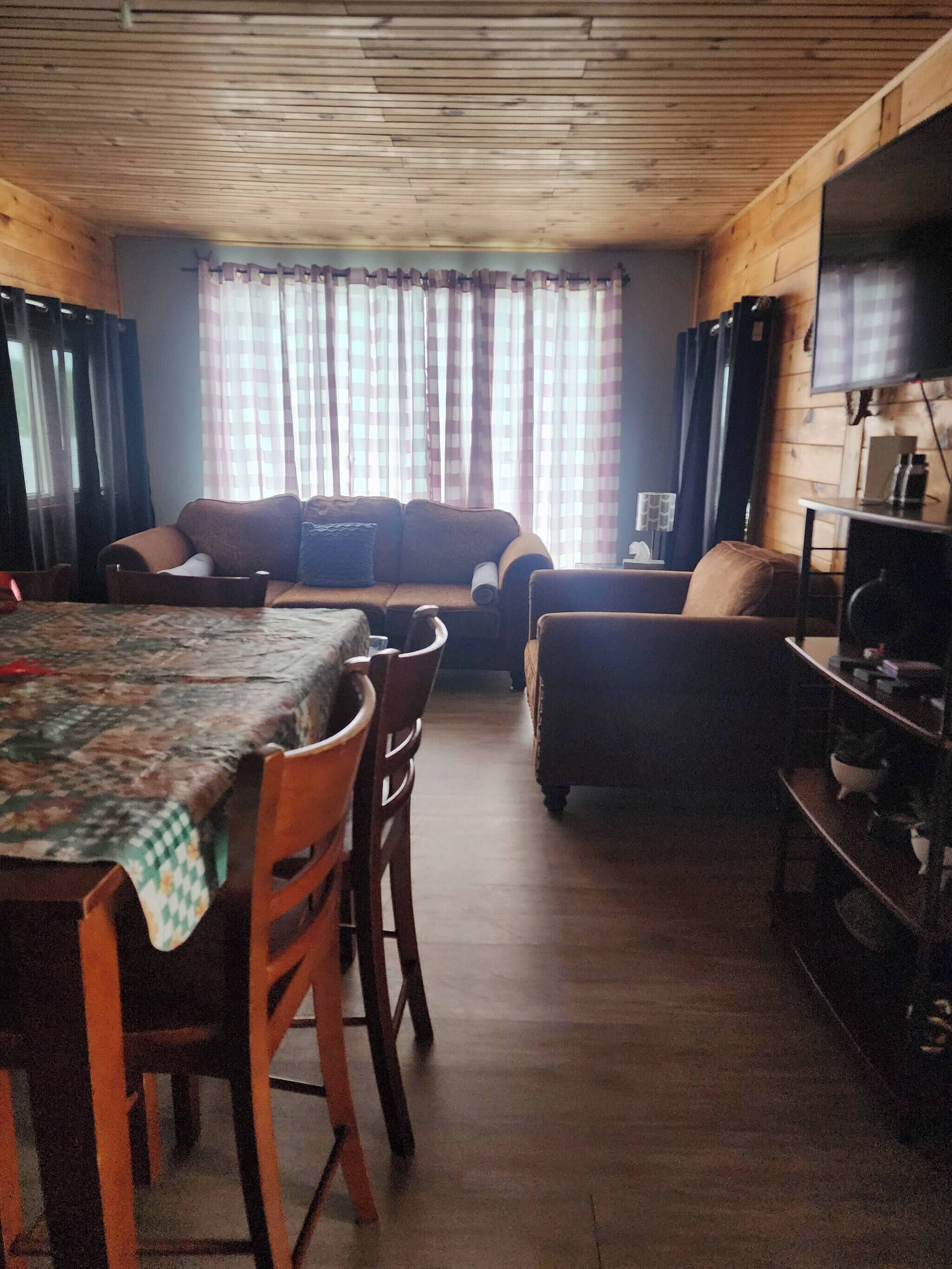 Un salon chaleureux avec un plafond en bois, un canapé, une table à manger avec des chaises et un téléviseur fixé à un mur en bois.