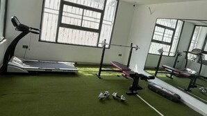 Une salle de sport équipée d’un tapis de course, d’un banc de musculation et d’haltères, le tout installé sur un sol vert.