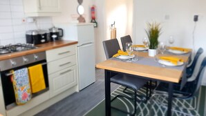 Ett modernt kök med vita skåp, en spis och ett litet kylskåp. Det finns ett matbord dukat med tallrikar, glas och en växt.