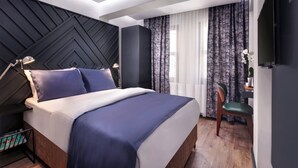 Camera d'albergo moderna con un letto grande, una scrivania con una sedia e un televisore montato a parete.