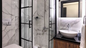 Un bagno moderno con doccia vetrata, parete rivestita in marmo, mobile lavabo in legno e uno specchio grande sopra il lavello.