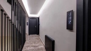 Un corridoio moderno con ringhiera in metallo nero, pavimento in marmo e una porta in fondo. Un display numerico digitale mostra "602".