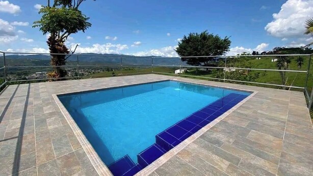 En rektangulær swimmingpool med blå fliser, omgivet af en flisebelagt terrasse.