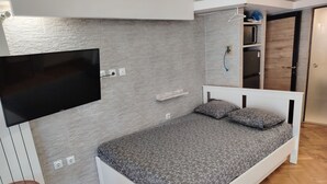 A bedroom with a bed, a TV mounted on the wall, a wardrobe, and a small table. - Waterfront Luxury Studio (Thessaloniki city)