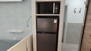 A compact kitchen with a built-in microwave and refrigerator, a wooden cabinet, and a small shelf. - Waterfront Luxury Studio (Thessaloniki city)