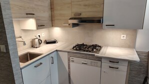 A compact kitchen with a gas stove, dishwasher, and a coffee maker. - Waterfront Luxury Studio (Thessaloniki city)
