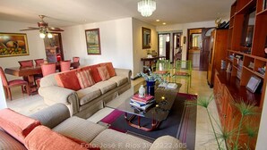 Ein Wohnzimmer mit Sofa, Couchtisch und Bücherregal. Es gibt einen Essbereich mit Tisch und Stühlen.