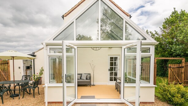 A modern house with a large glass front, a dining area with outdoor furniture, and a garden. - Rural Norfolk Cottage welcoming 3 dogs (Hickling)