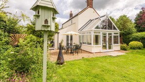 A house with a conservatory, a patio with outdoor furniture, and a garden with various plants. - Rural Norfolk Cottage welcoming 3 dogs (Hickling)