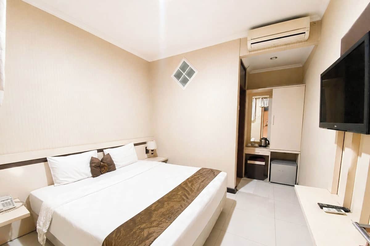 A hotel room with a bed, bedside table, lamp, air conditioning unit, and a TV.