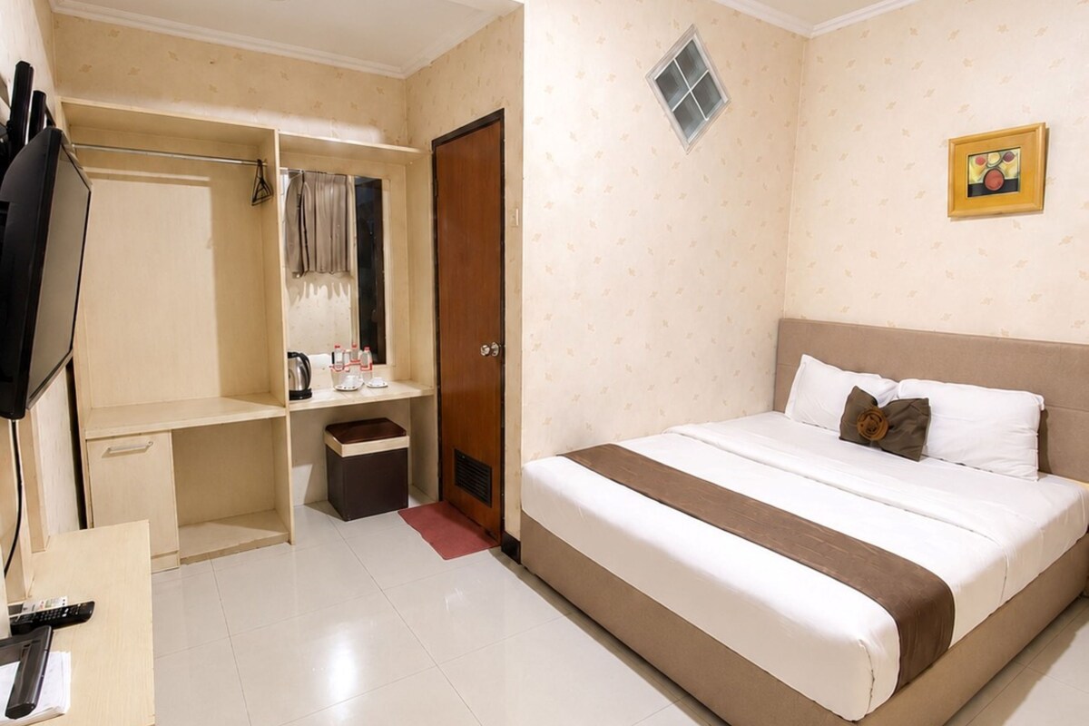 A hotel room with a bed, a desk, a wardrobe, and a television.