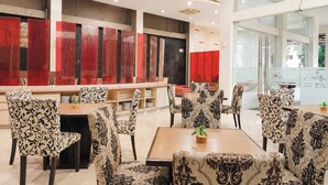 A modern restaurant with patterned chairs and tables, a counter with red panels, and a glass partition. - Scarlet Hotel Stasiun Bandung (Bandung)