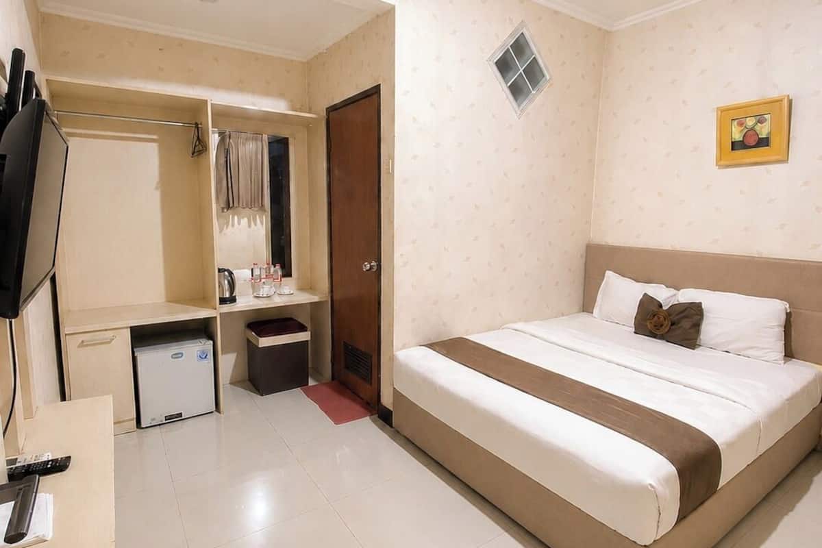 A hotel room with a bed, a desk, a wardrobe, a small kitchenette, and a television.