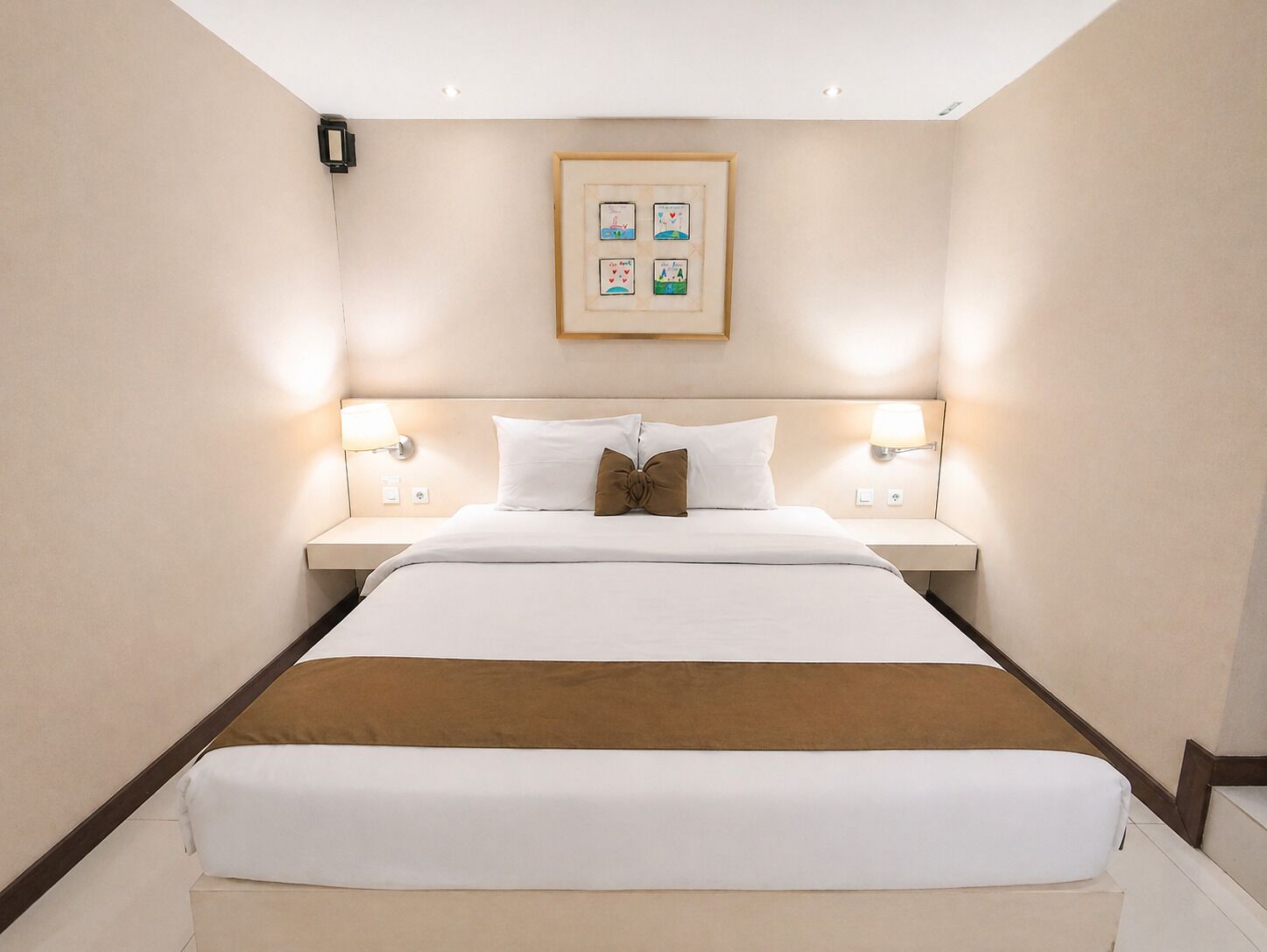Een hotelkamer met een groot bed, twee bedlampen, een lijst met een afbeelding aan de muur en een houten hoofdbord.