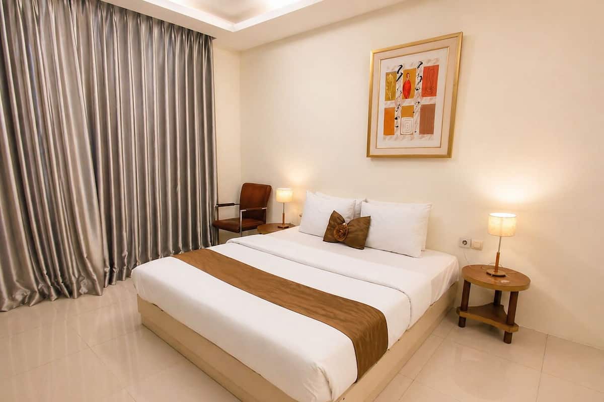 A hotel room with a large bed, two bedside tables, a chair, a lamp, and a framed picture on the wall.