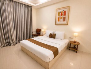 Una habitación de hotel con una cama grande, dos mesitas de noche, una silla, una lámpara y un cuadro en la pared.