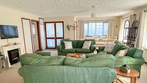 A living room with green sofas, a fireplace, a television, and a dining area with a table and chairs. - Hideaway near the sea - sleeps 6 guests & welcomes 2 dogs (Scratby)