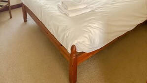 A neatly made bed with white linens and towels, a wooden headboard, a nightstand with a lamp, and a window with curtains. - Hideaway near the sea - sleeps 6 guests & welcomes 2 dogs (Scratby)