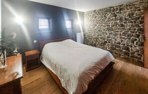 A bedroom with a bed, a nightstand, a lamp, and a stone wall. - Jolie maison avec piscine (Hestrud)