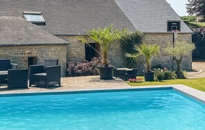 Ein Schwimmbeckenbereich mit Steinmauern, Sitzgelegenheiten im Freien und Topfpflanzen.
